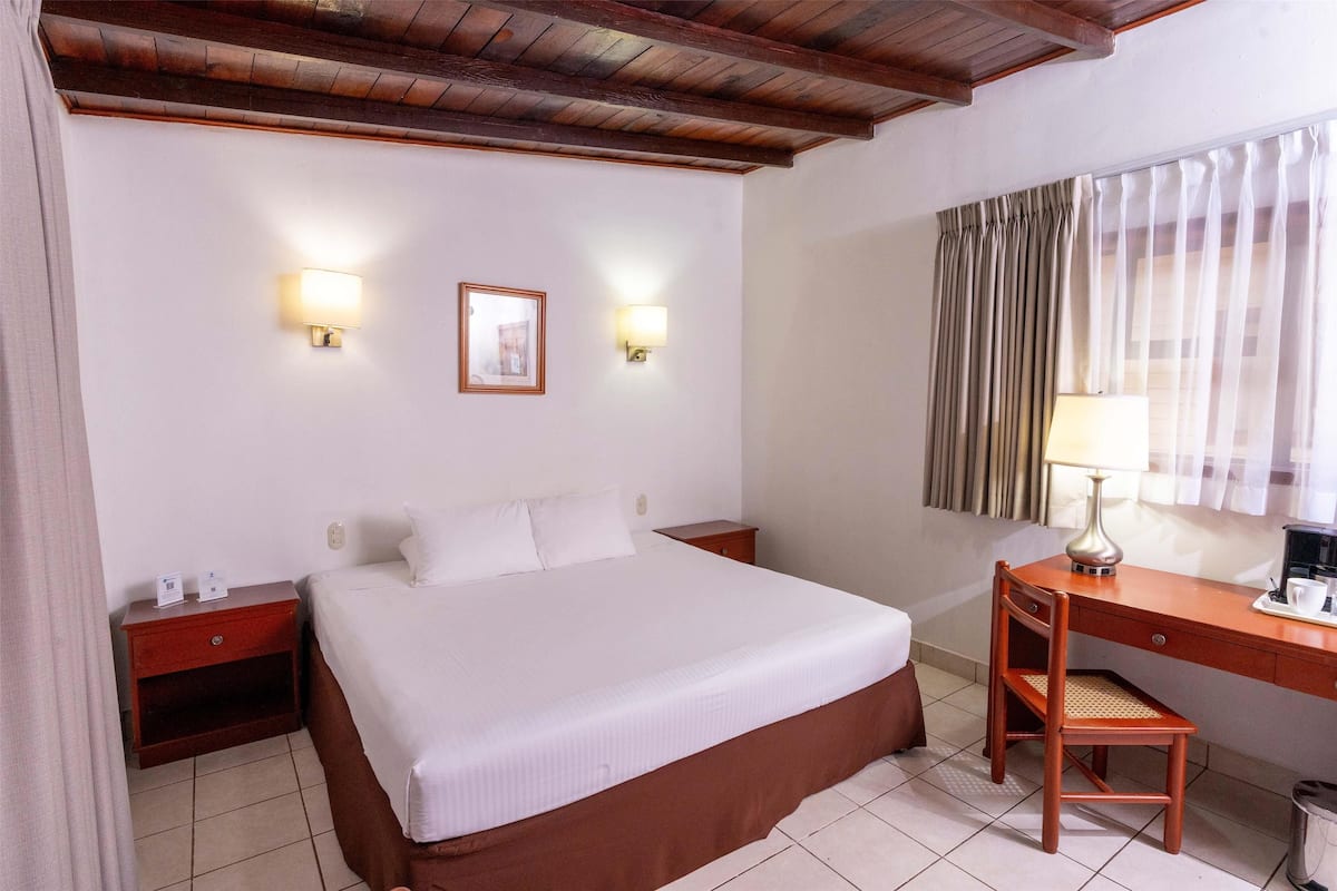 Habitación de hotel con una cama grande, mesitas de noche, un escritorio con una silla y dos lámparas de pared.