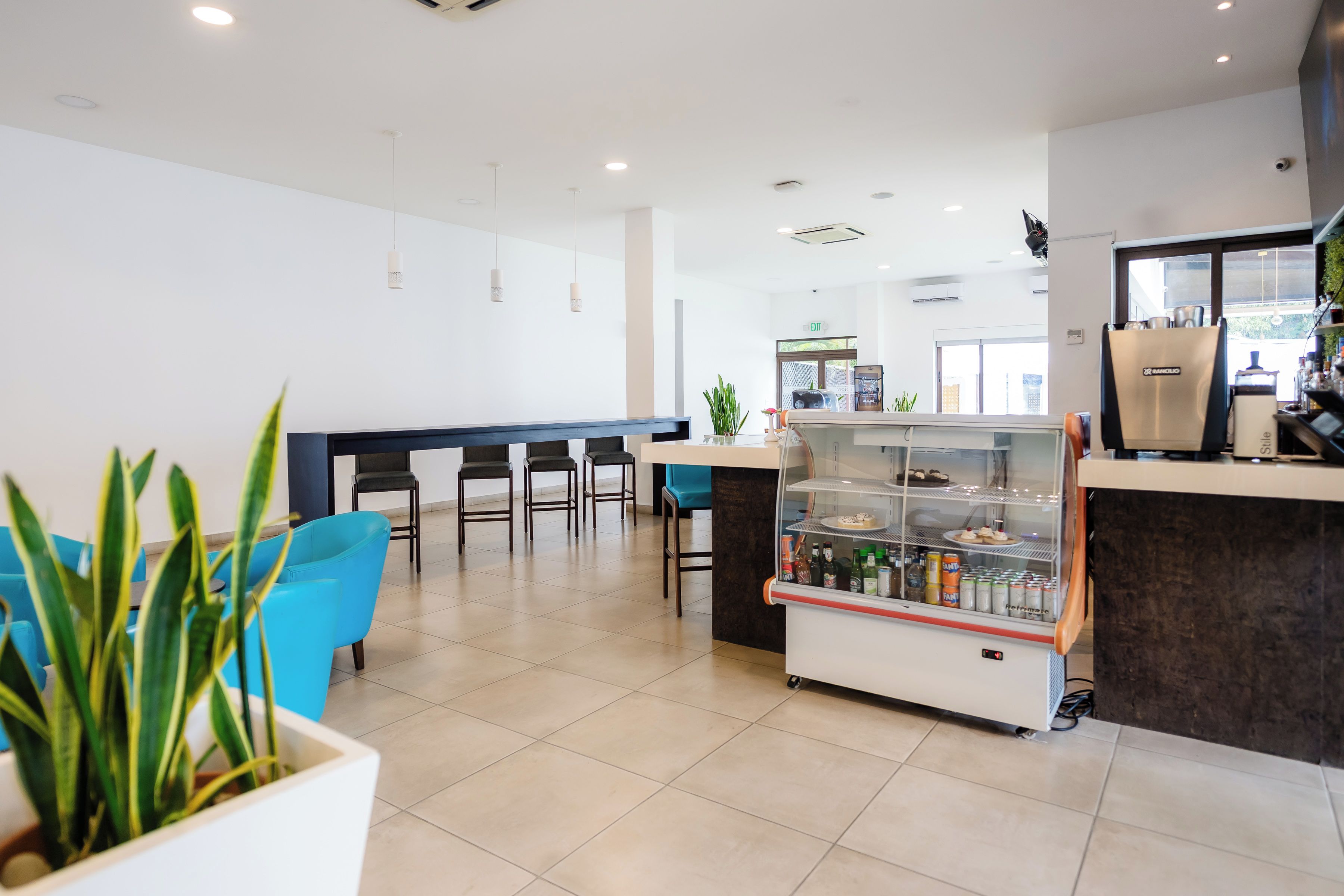 Un intérieur moderne comprenant un espace salon, un comptoir avec un distributeur de boissons et un panneau de signalisation indiquant la sortie.