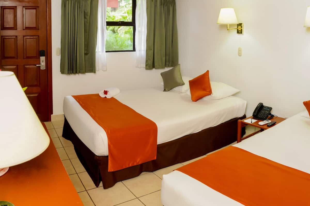 Habitación de hotel con dos camas, una mesita de noche con teléfono y control remoto, una ventana con cortinas y una puerta.