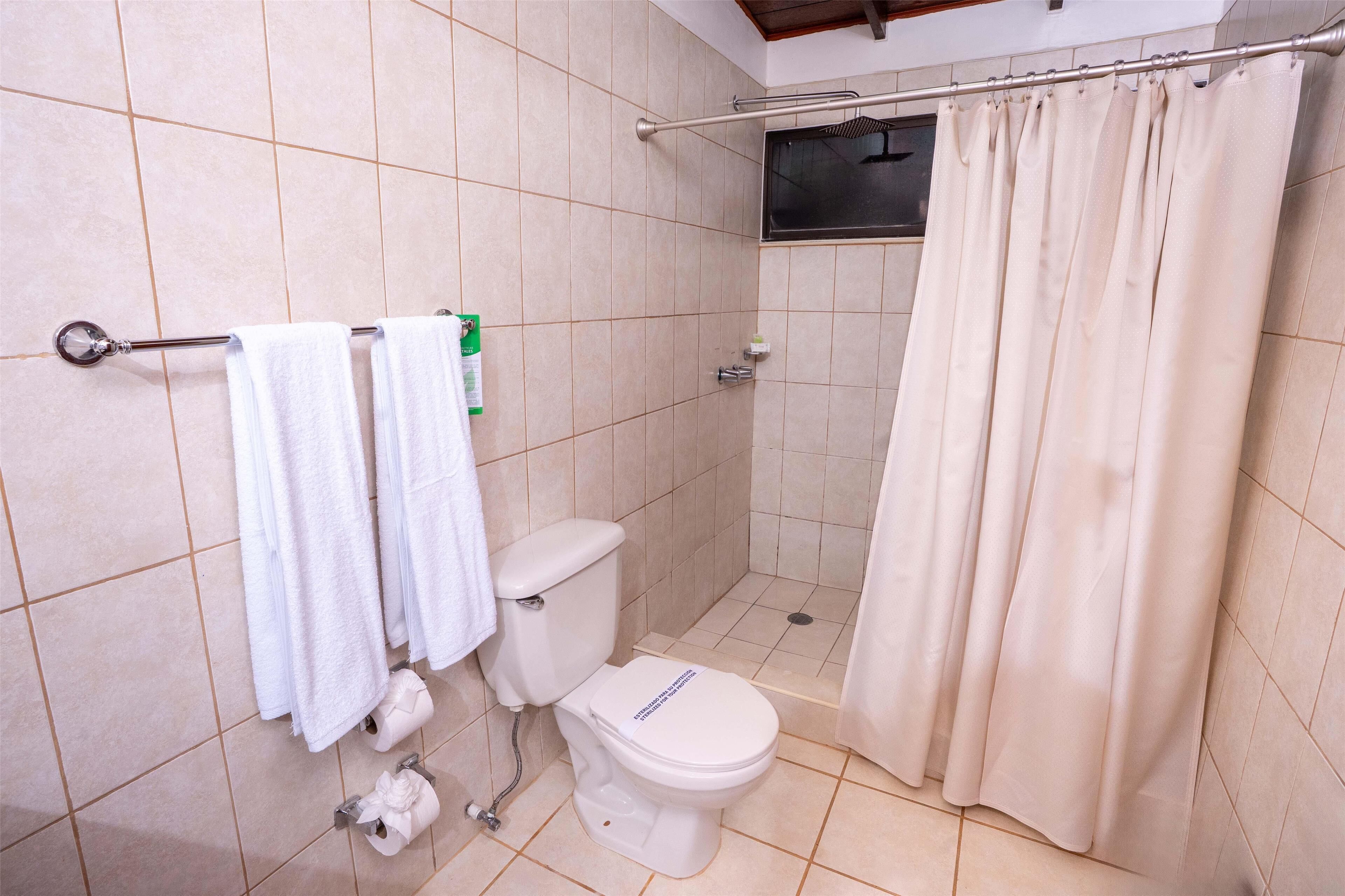A bathroom with a toilet, a shower curtain, and a towel rack with towels.