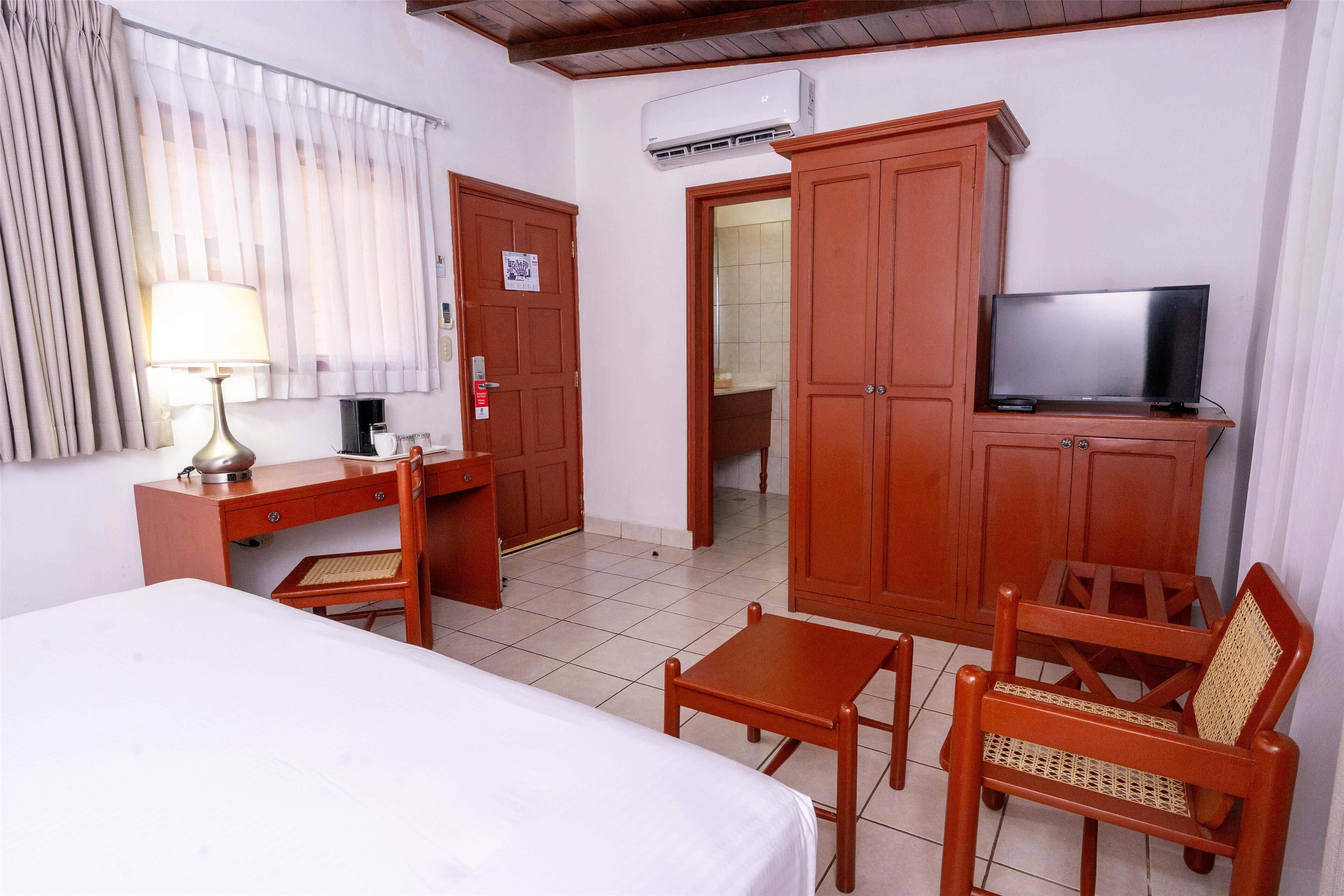 A hotel room with a bed, desk, chair, television, and wardrobe.