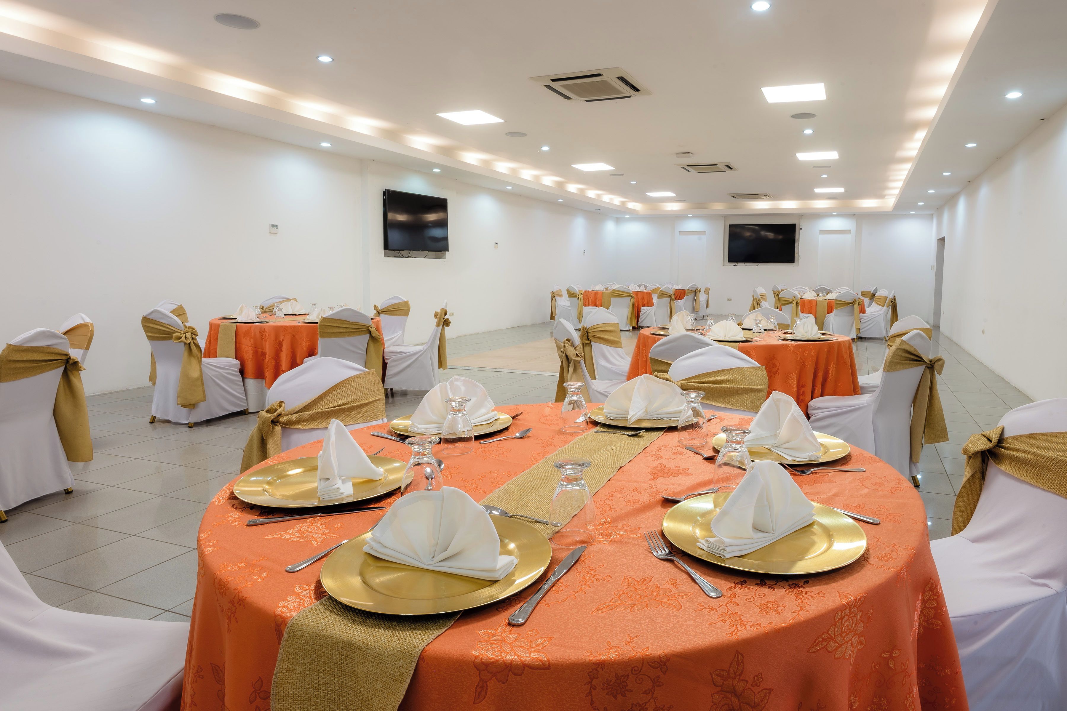A conference room with tables set for a formal event, equipped with chairs, tables, and a flat-screen TV.