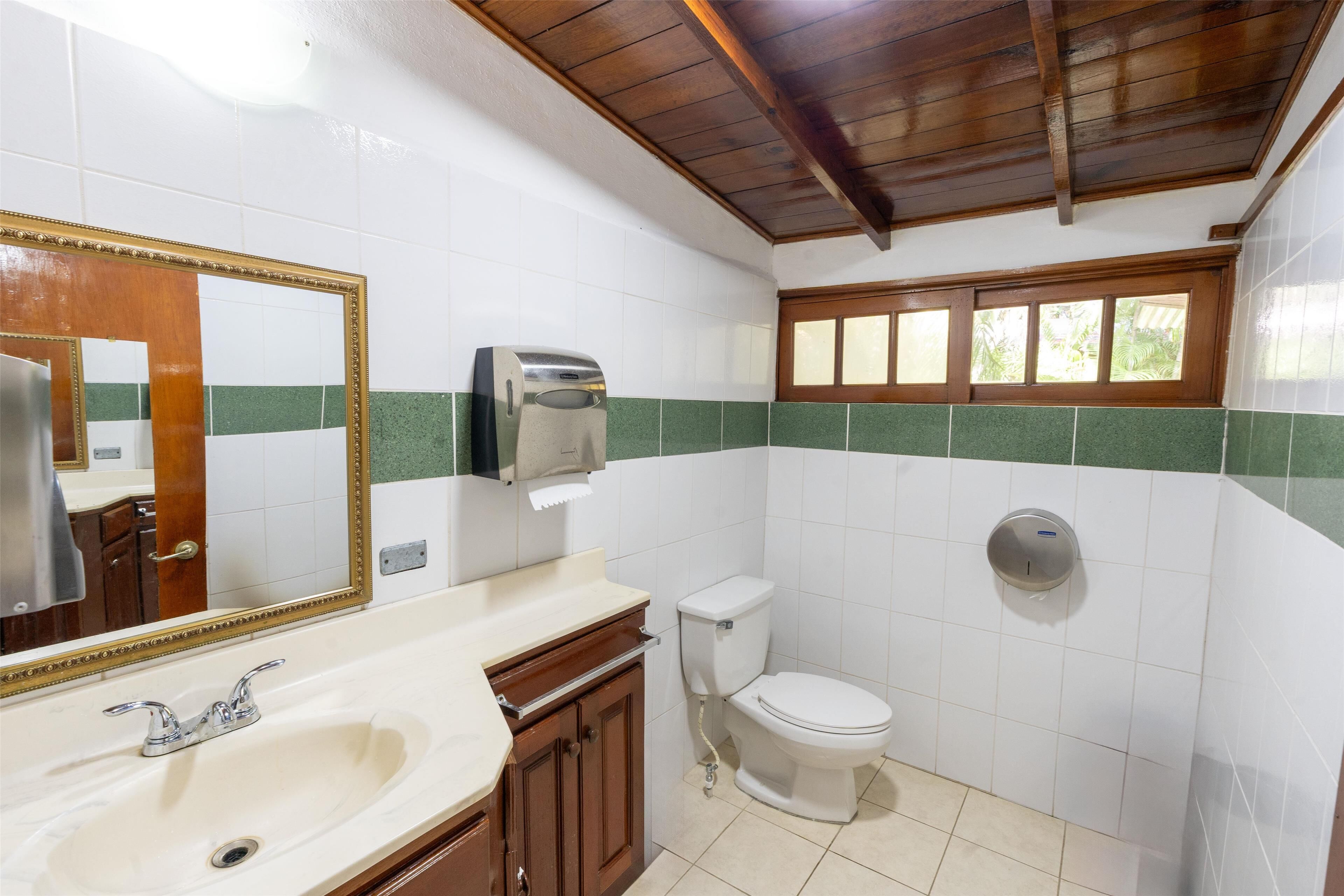 A bathroom with a sink, mirror, toilet, and a window.