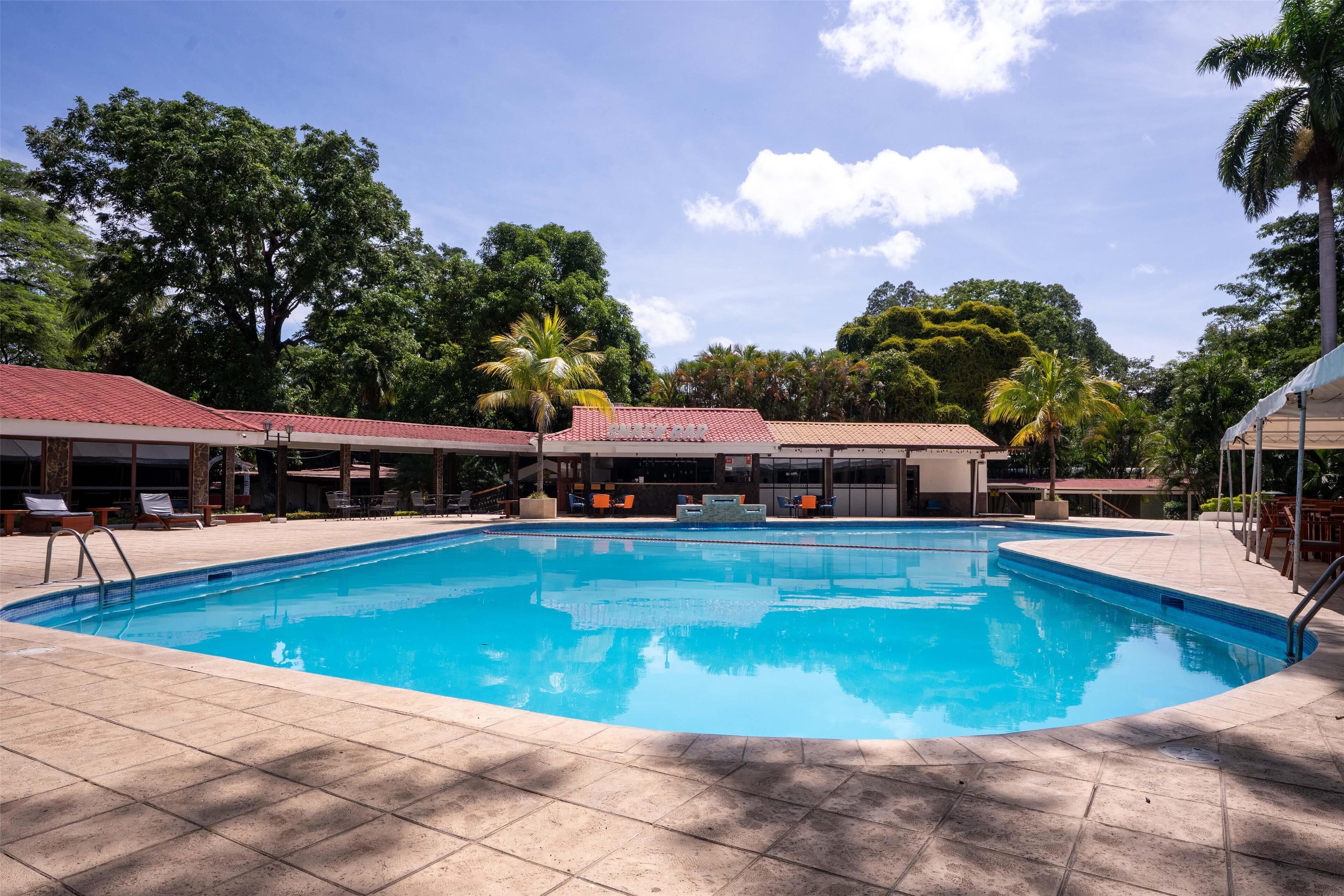 A swimming pool with tiled deck, lounge chairs, and covered seating areas.