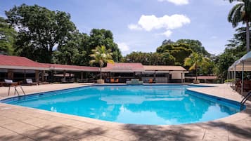 A swimming pool with tiled deck, lounge chairs, and covered seating areas.