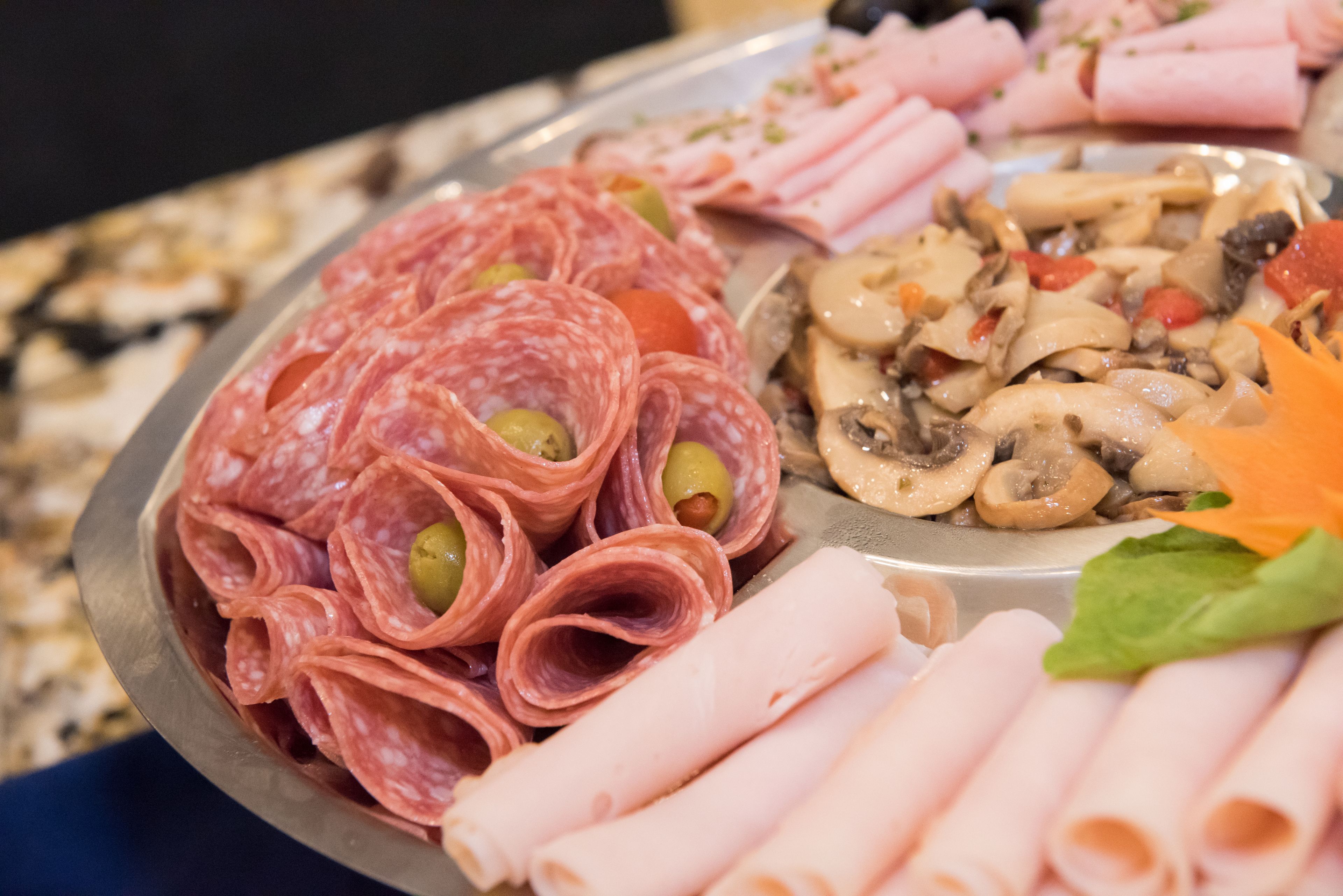 Un piatto assortito di salumi e carni, con prosciutto a fette, salame e funghi.