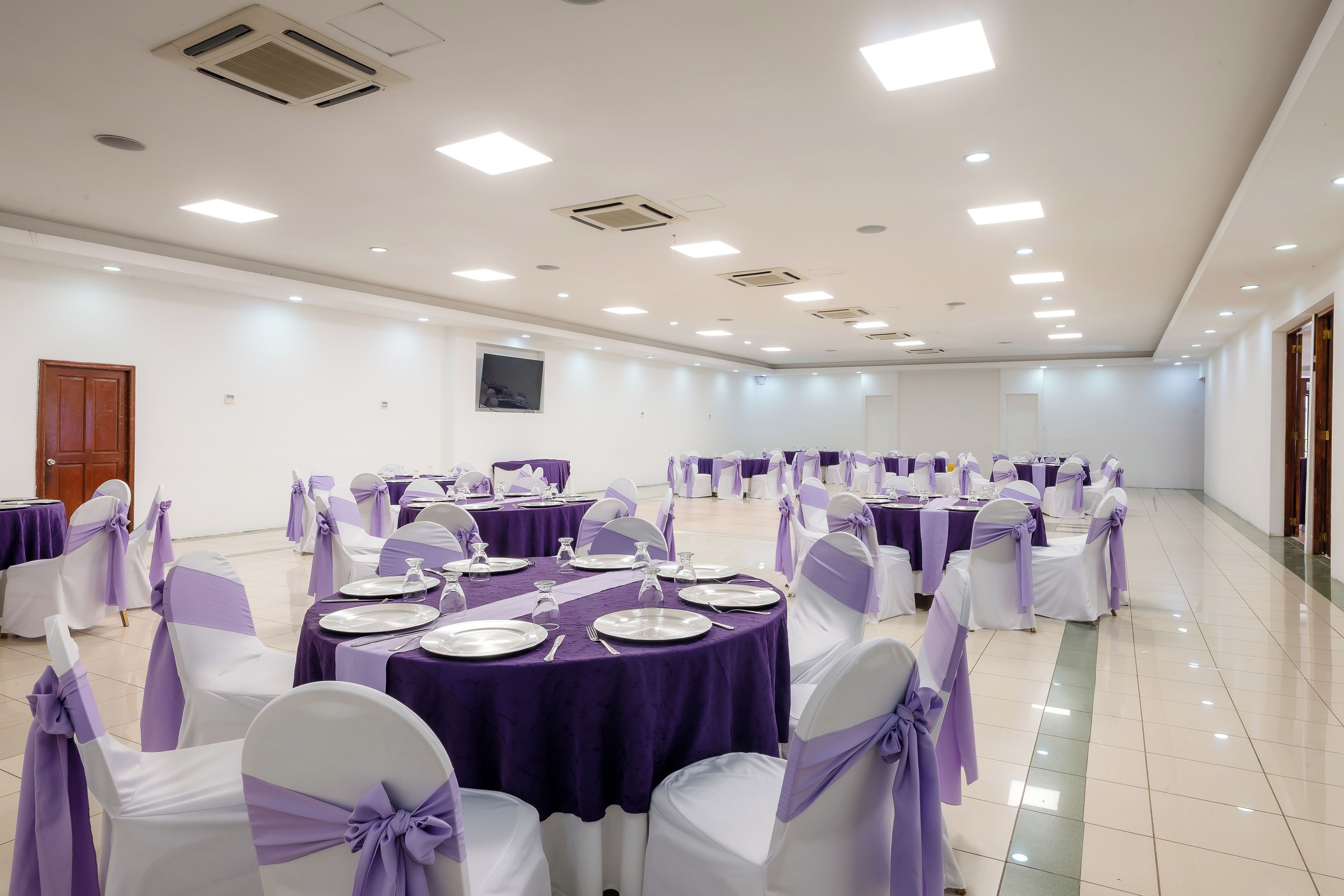 Ein Festsaal mit runden Tischen, weißen Stühlen mit violetten Bändern und einem gefliesten Boden.