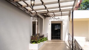 Un pasaje cubierto que lleva al Restaurante La Pérola, con barandilla de metal y plantas en macetas.