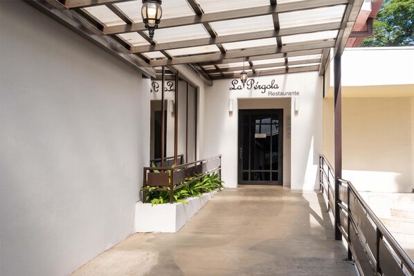 A covered walkway leading to a restaurant entrance with a metal railing and potted plants. - Best Western Las Mercedes Airport (Managua)