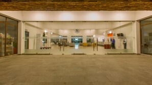 Un vestíbulo amplio con diseño moderno, que cuenta con un techo alto con ladrillo a la vista, un candelabro central y una entrada de vidrio hacia la zona de recepción.