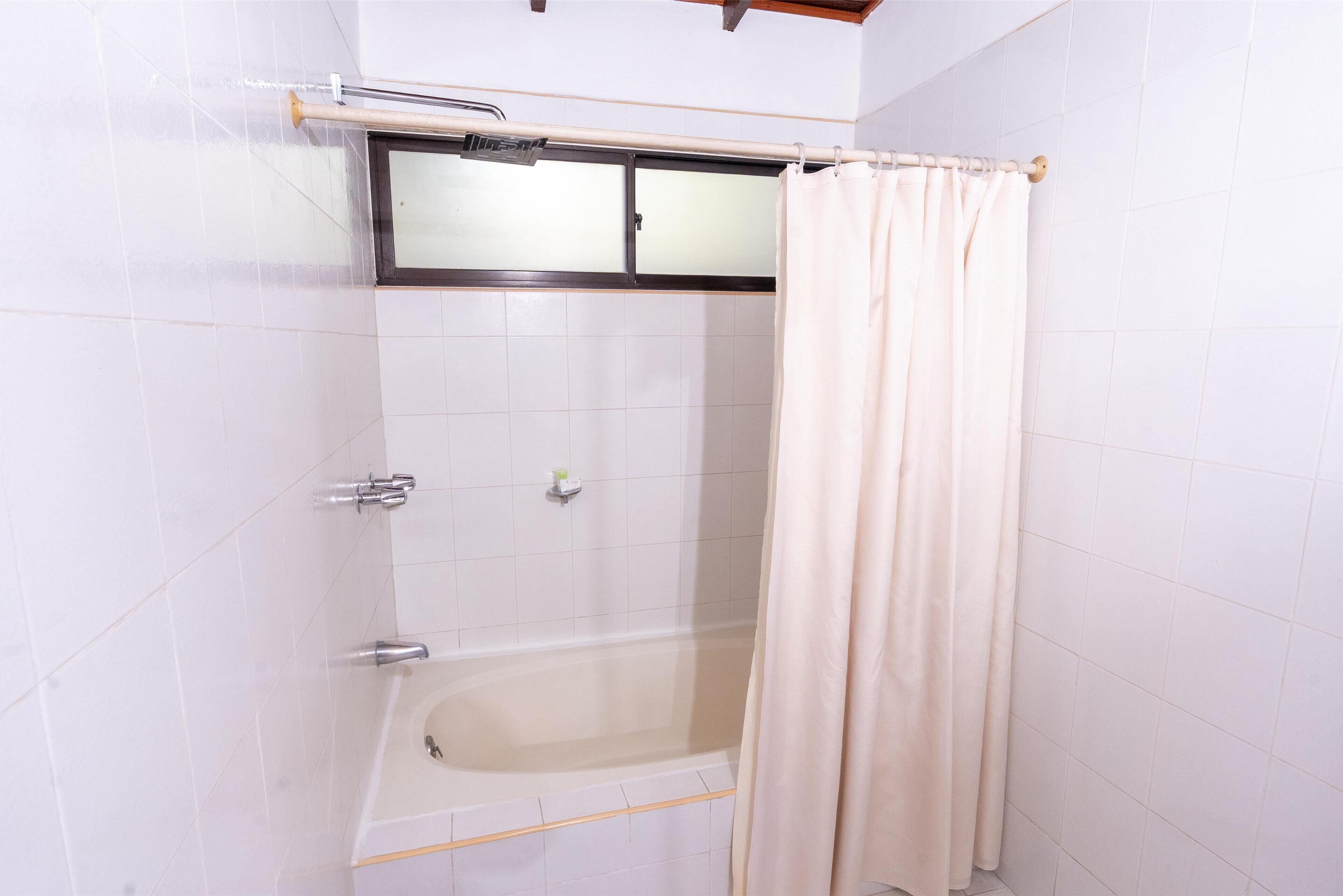 A bathroom with a bathtub, a shower curtain, and a window with a frosted glass panel.