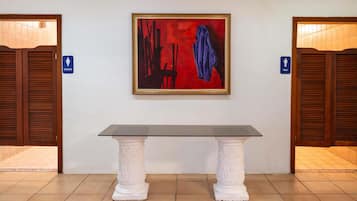 A hallway with a framed abstract painting, a glass-top table, and doors marked for men and women.