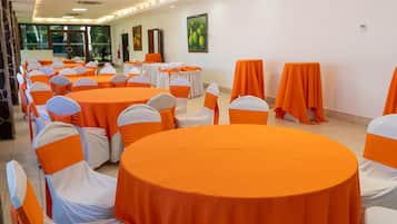 A conference room with round tables covered in orange tablecloths and white chairs with orange sashes.