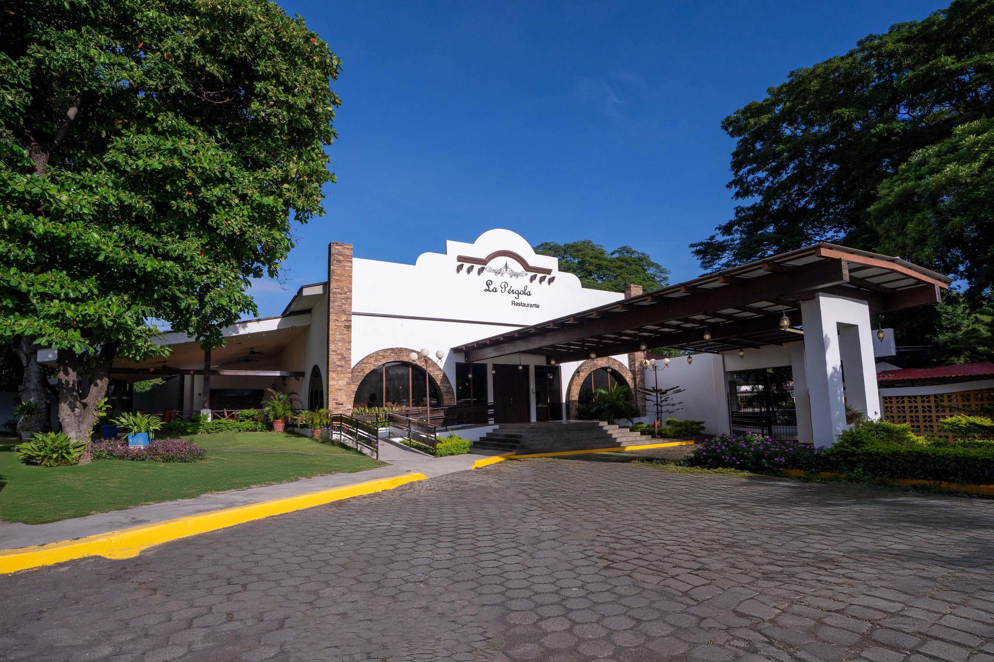 Un edificio con un letrero que dice "La Perola Restaurante", con una entrada cubierta y un camino de entrada pavimentado.