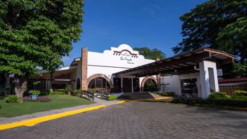 A building with a sign reading "La Perola Restaurante" with a covered entrance and a paved driveway.