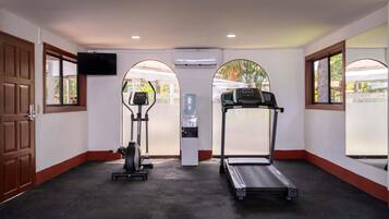 Une salle de sport équipée de matériel d’exercice, d’un distributeur d’eau et d’un téléviseur fixé au mur.