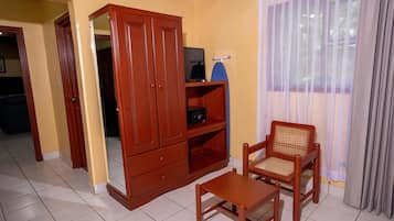 A room with a wooden cabinet, a television on a shelf, a wicker chair, and a window with curtains.