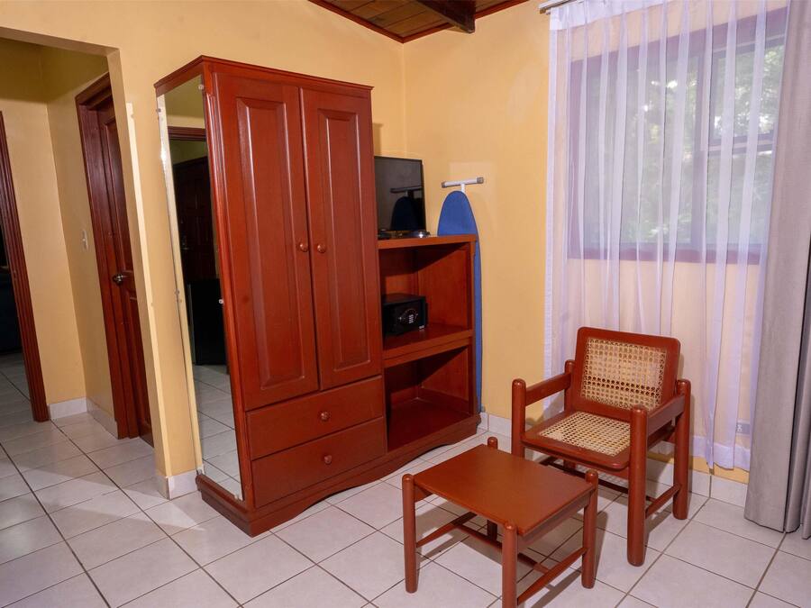 A room with a wooden cabinet, a television on a shelf, a wicker chair, and a window with curtains.