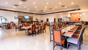 Un grand espace dédié à la salle à manger, avec plusieurs tables et chaises, un comptoir de bar et un écran de télévision.