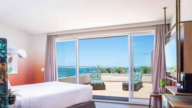 A hotel room with a bed, a desk, a TV, and a balcony with a view of the sea. - Mercure Rio Boutique Hotel Copacabana (Rio de Janeiro)