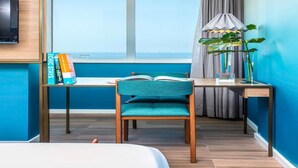 A room with a bed, a desk with a chair, a TV, a window with a view of the sea, and a plant. - Mercure Rio Boutique Hotel Copacabana (Rio de Janeiro)