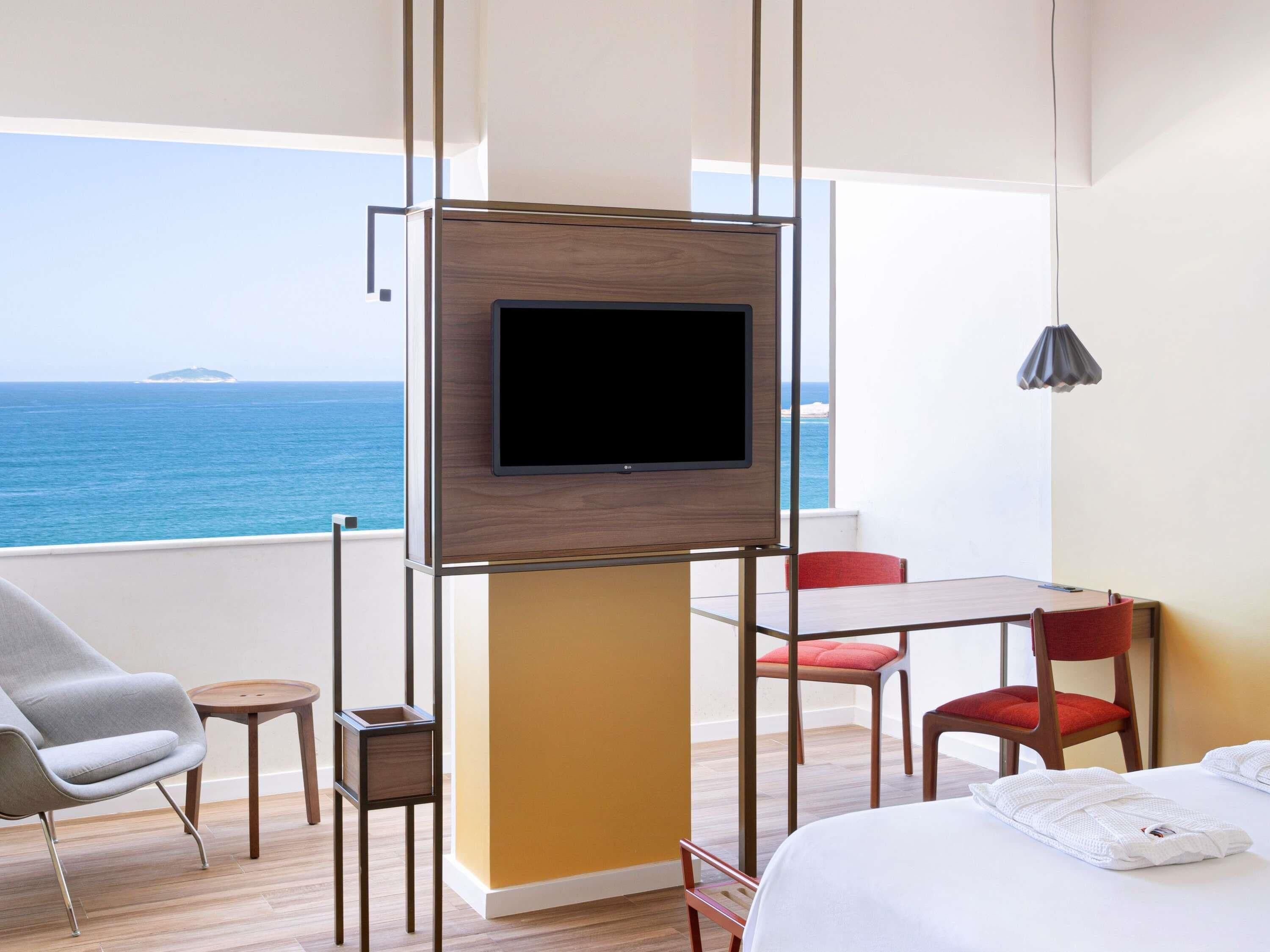 Une chambre d’hôtel équipée d’une télévision, d’un lit, d’une table, de deux chaises et offrant une vue sur la mer.
