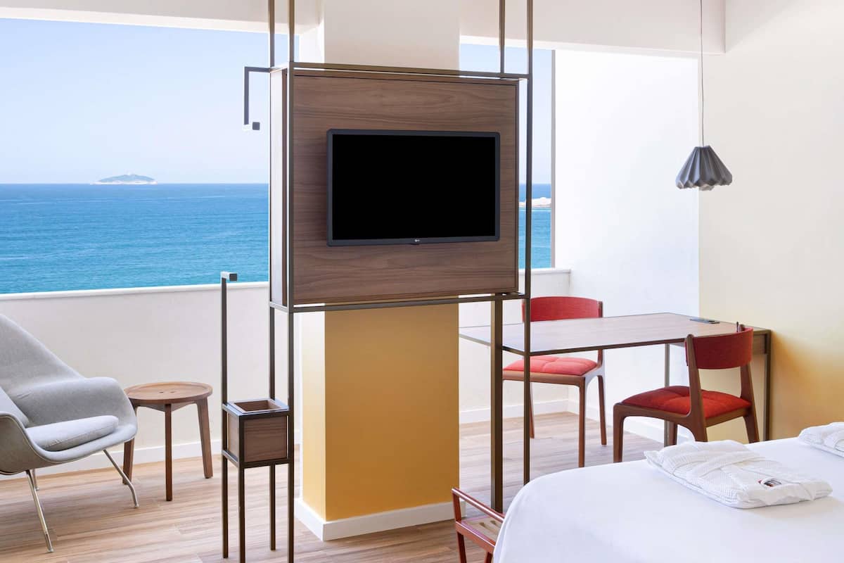 A hotel room with a TV, a bed, a table, two chairs, and a view of the sea.