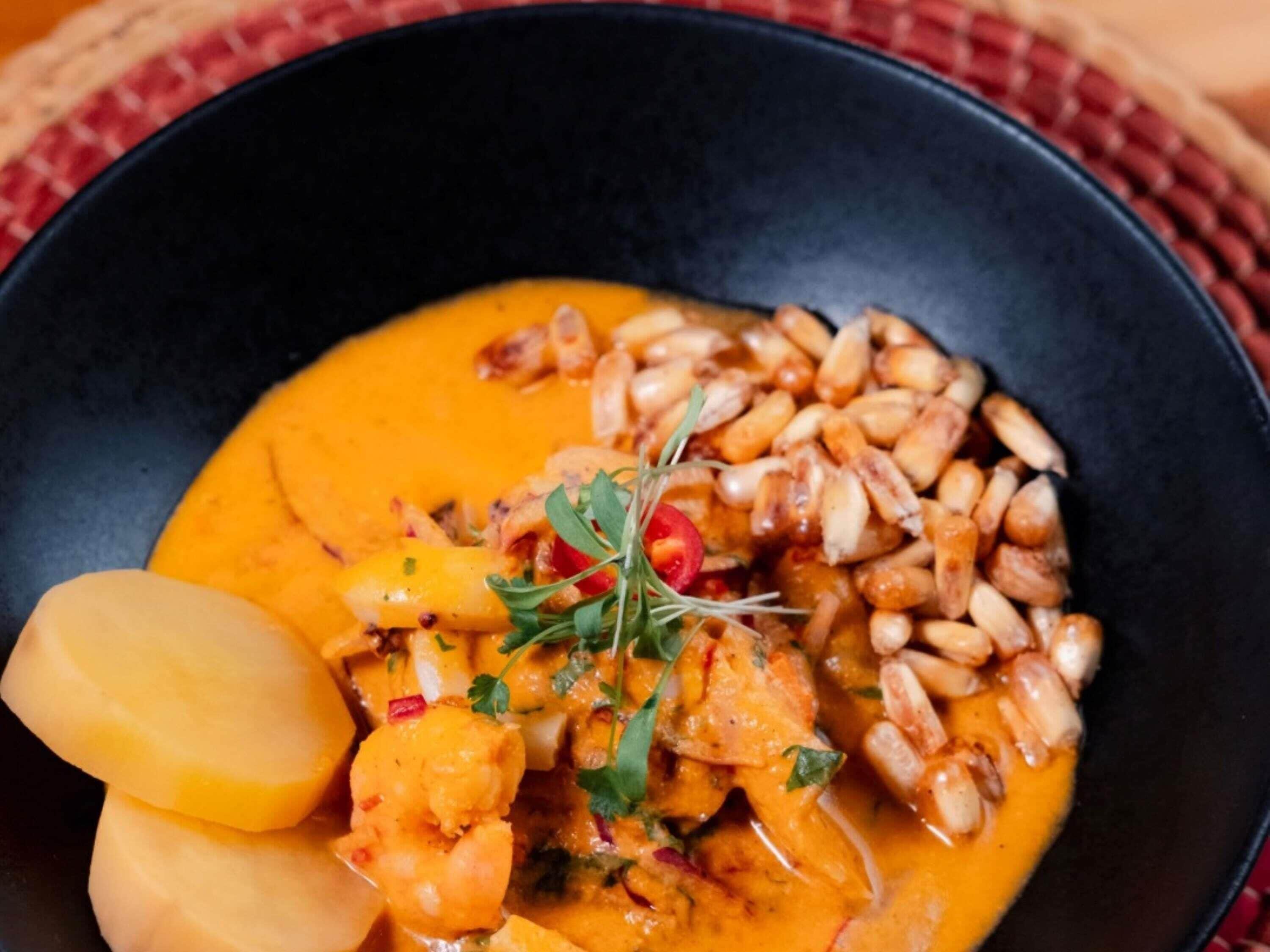 A bowl of food with a creamy sauce, peanuts, and garnishes.