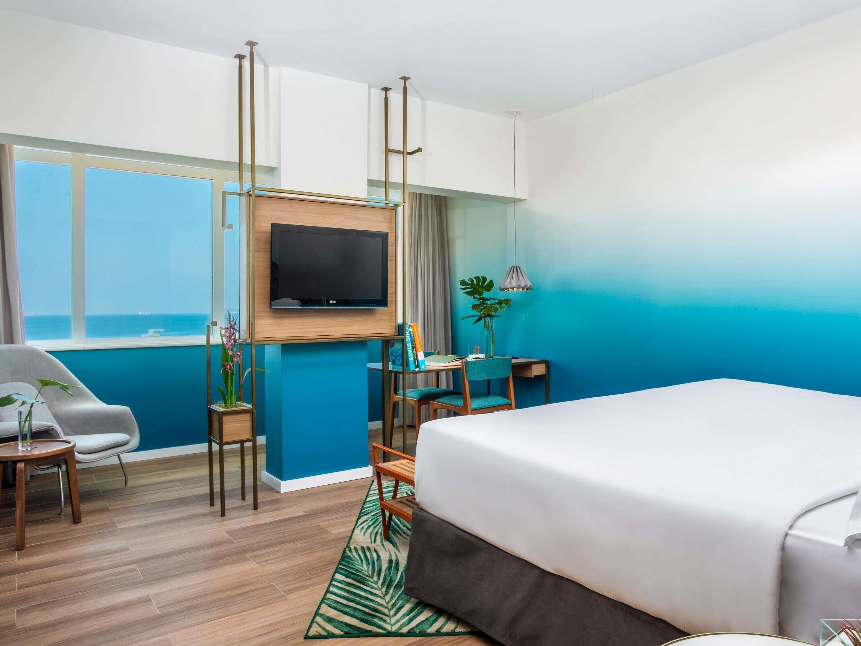 Habitación de hotel con cama, escritorio, silla, televisor en la pared y vista al mar.