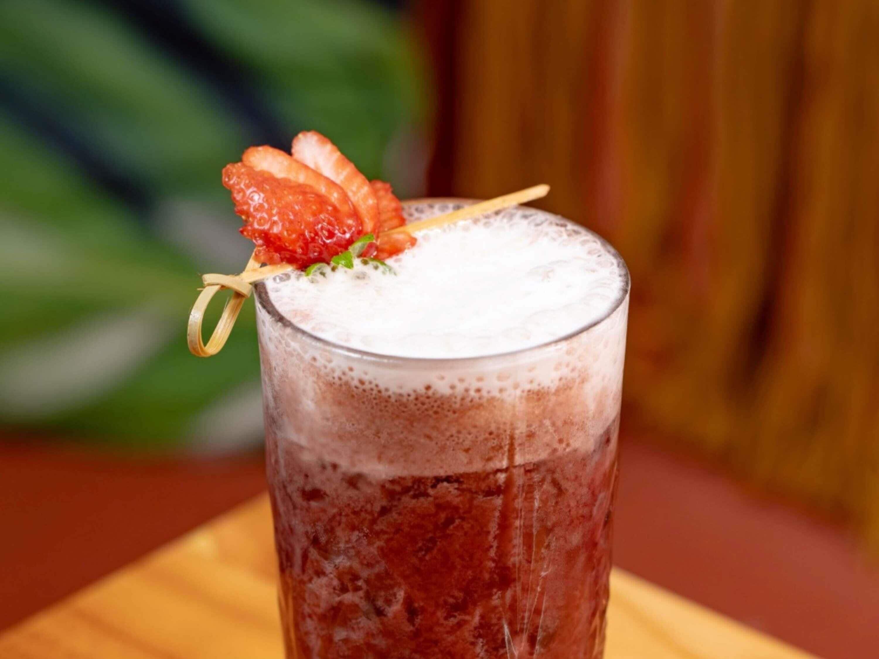 A glass of beverage with a strawberry garnish on a wooden surface.