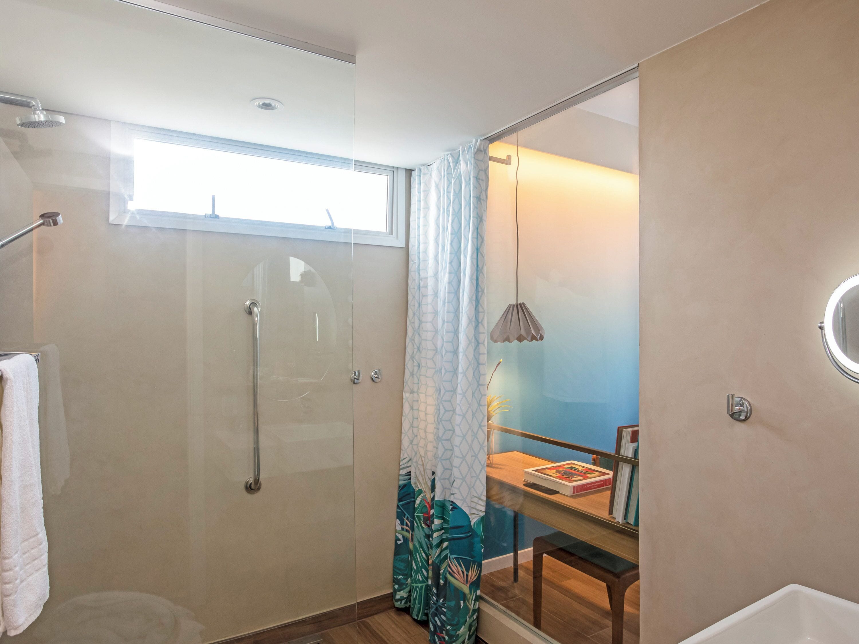 A modern bathroom with a glass shower enclosure, a towel rack, a small table with books, and a pendant light.