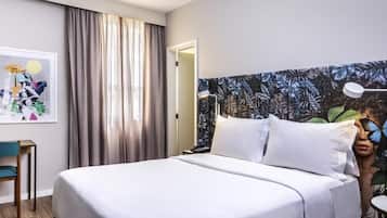A hotel room with a bed, a desk, a chair, and a wall with a leaf pattern.