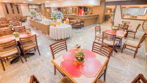 A spacious dining area with multiple tables and chairs, a central bar area, and a view of the kitchen through a glass partition. - Hotel Dan Inn Uberaba & Convenções by Nacional Inn (Uberaba)