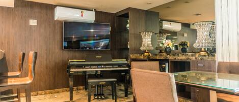 Una sala de estar moderna con un piano, un televisor de pantalla plana y una mesa de comedor de vidrio con sillas.