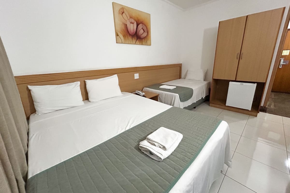 Una habitación de hotel con una cama grande, una cama más pequeña, un armario, un escritorio y un cuadro en la pared.