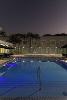 Una piscina con escalera metálica, rodeada por un edificio con múltiples ventanas y una zona de estar cubierta.