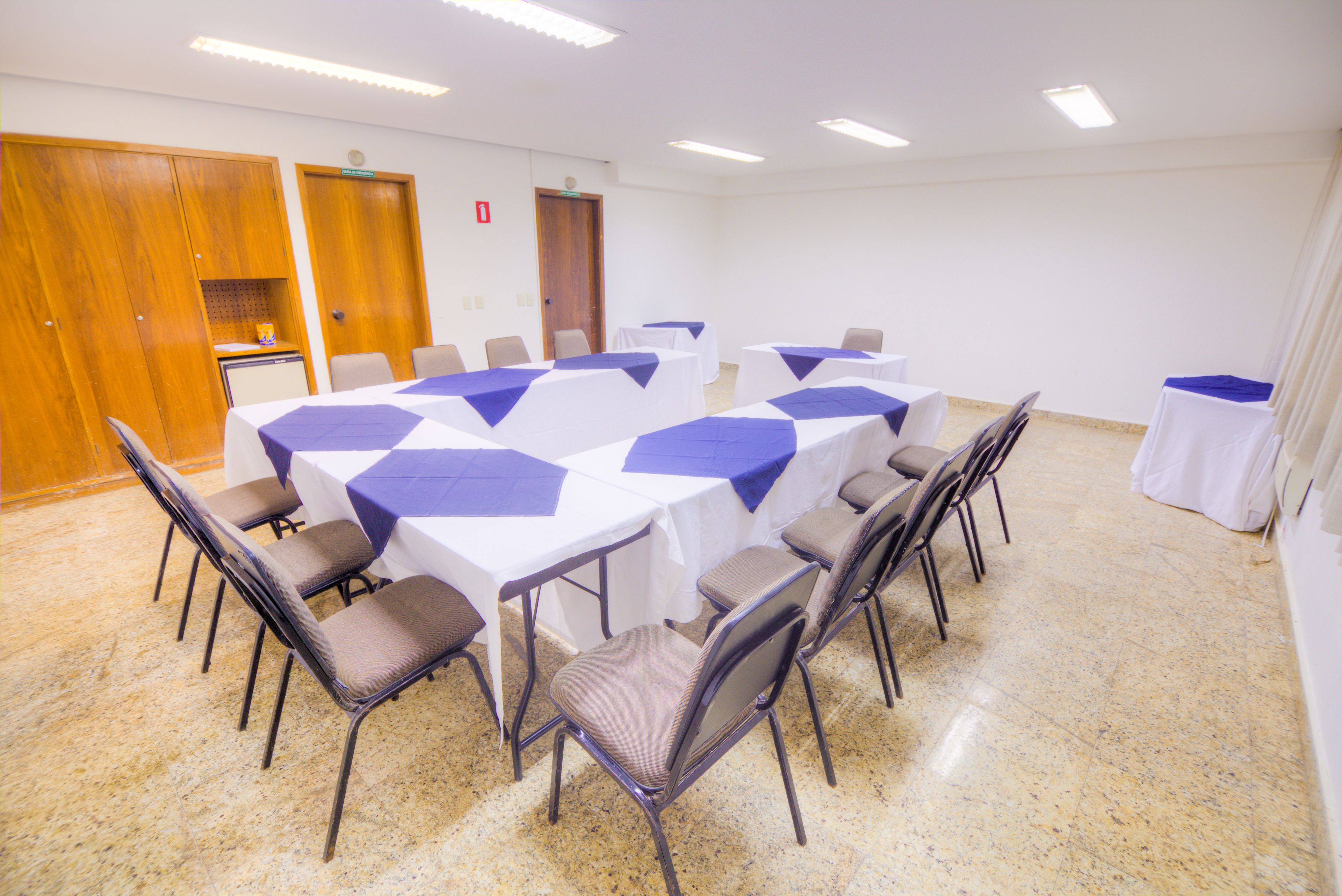 A conference room with a large oval table surrounded by chairs, white tables with blue tablecloths, and a wooden cabinet.
