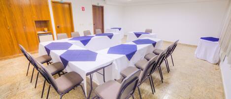 A conference room with a large oval table surrounded by chairs, white tables with blue tablecloths, and a wooden cabinet.