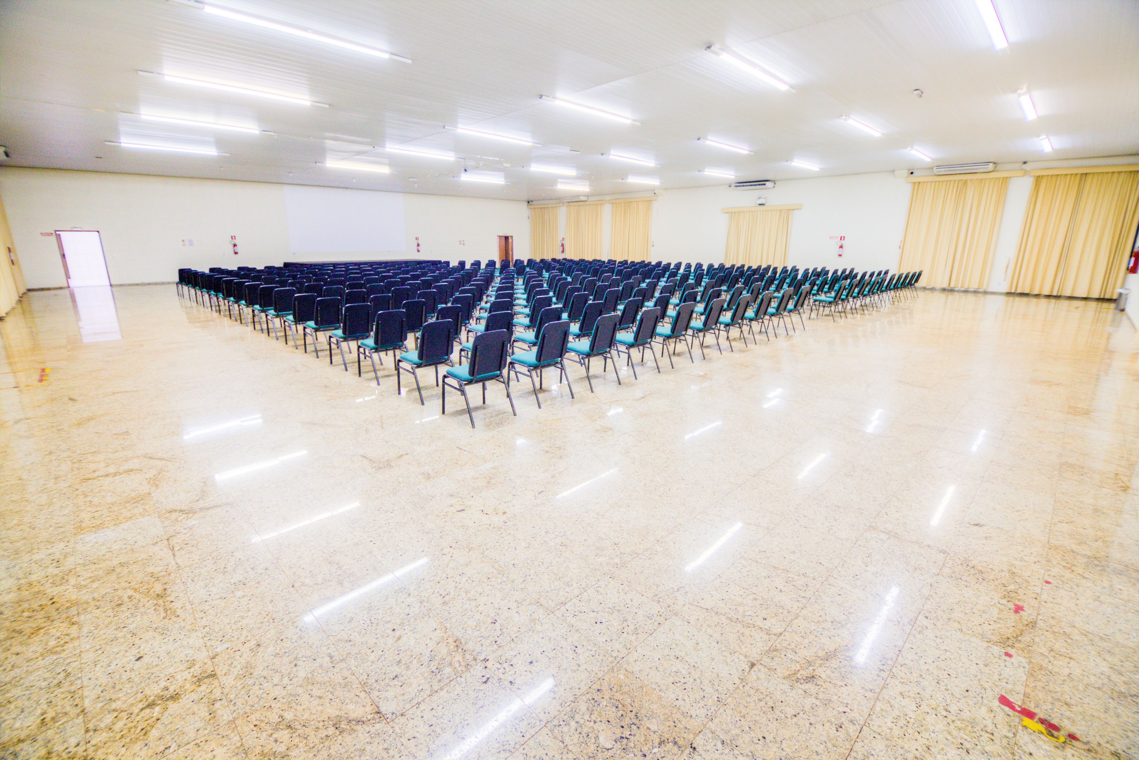 A large hall with rows of chairs, a stage, and a whiteboard.