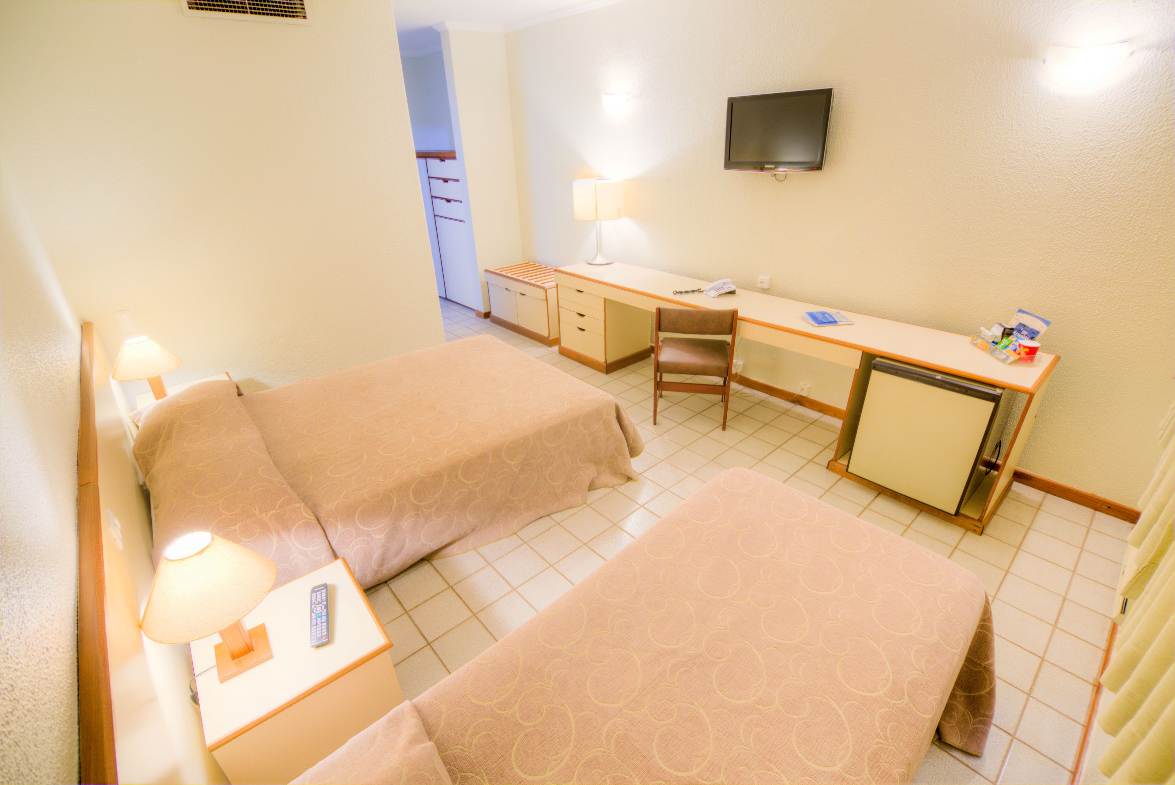 A hotel room with two beds, a desk, a chair, a TV, and a lamp.