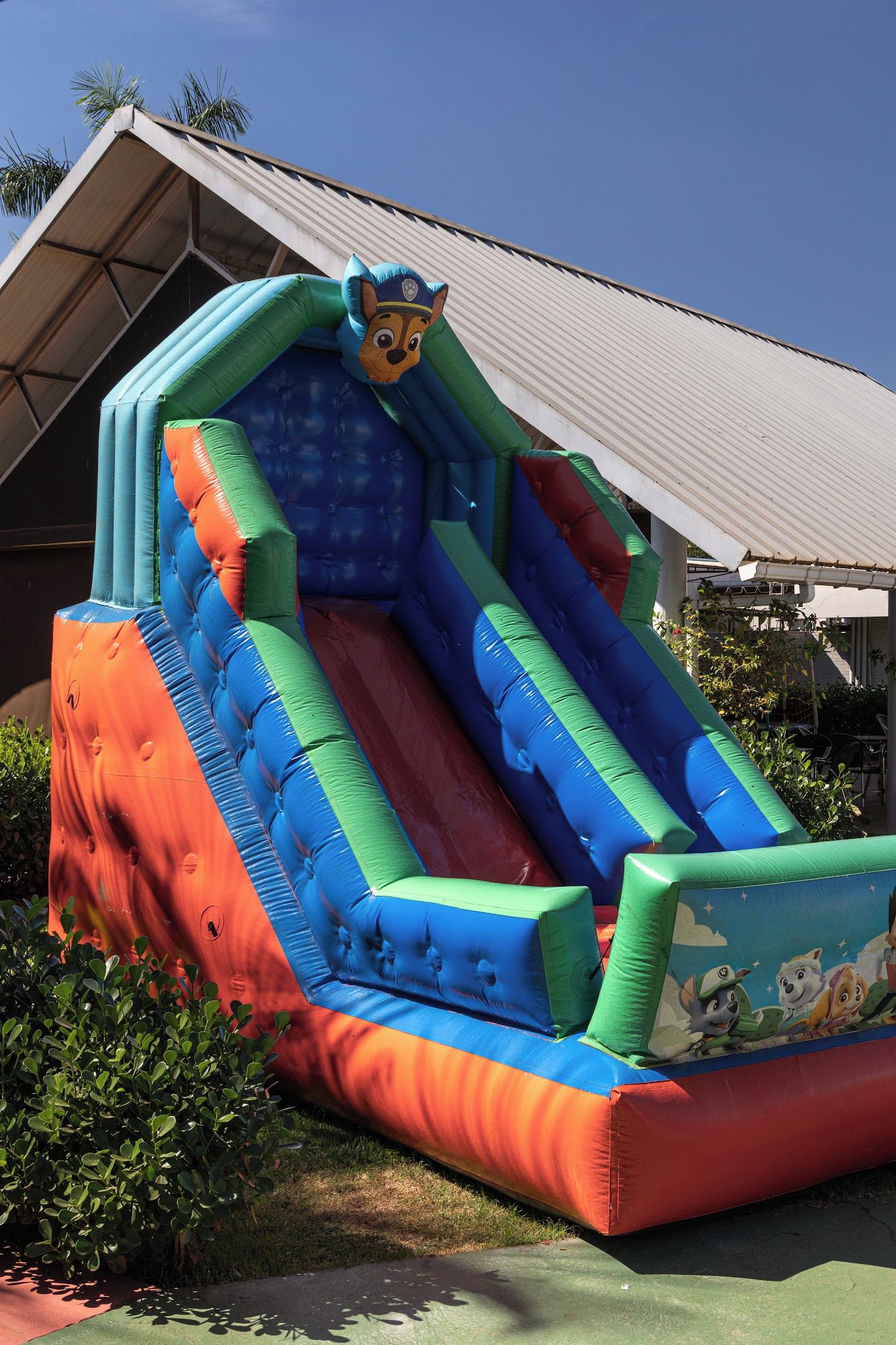 Un tobogán inflable con diseño de personaje de caricatura, frente a un edificio con techo inclinado.