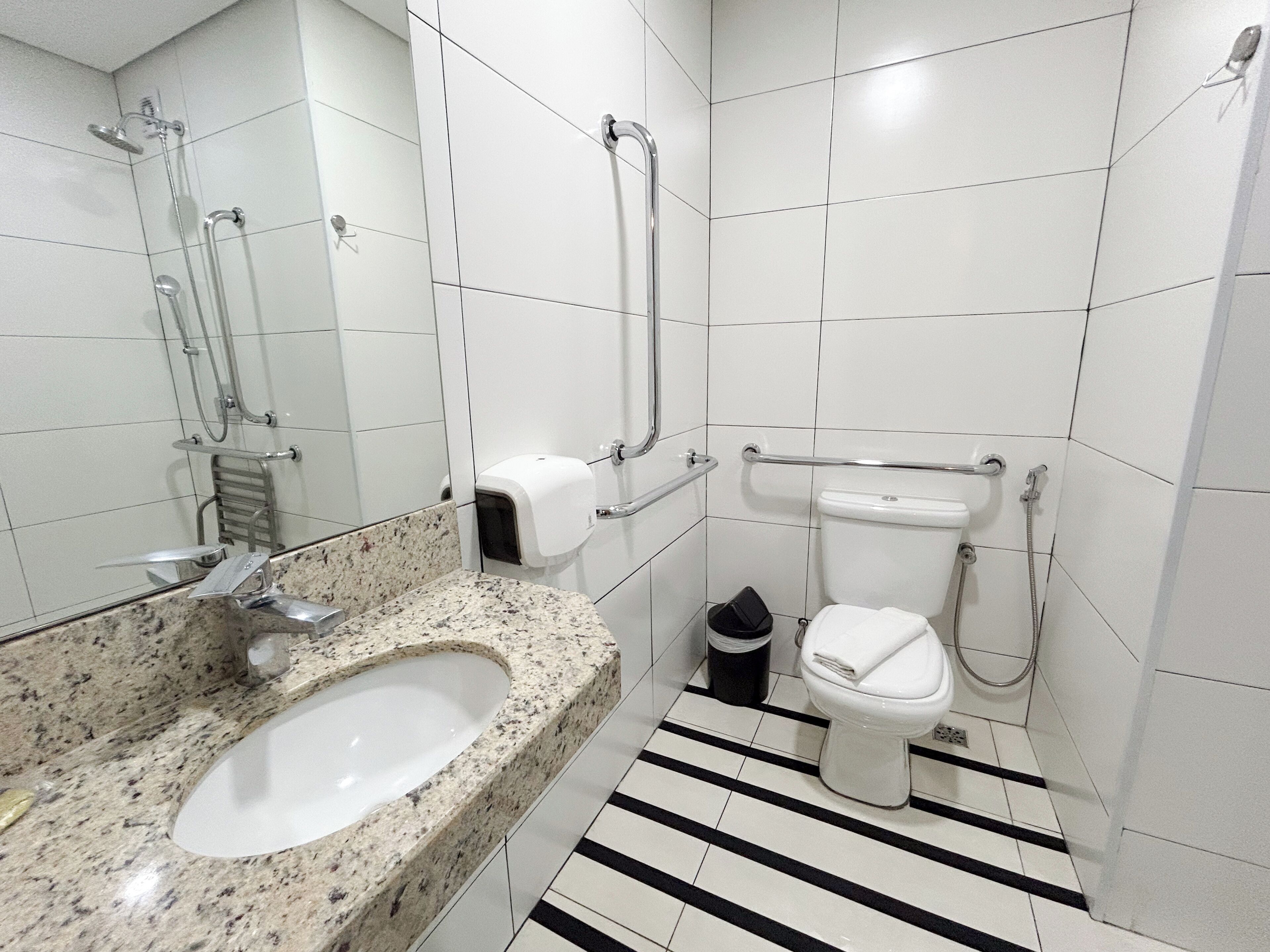 Un baño moderno con lavamanos de granito, inodoro con barra de apoyo y ducha con cabezal de ducha manual.