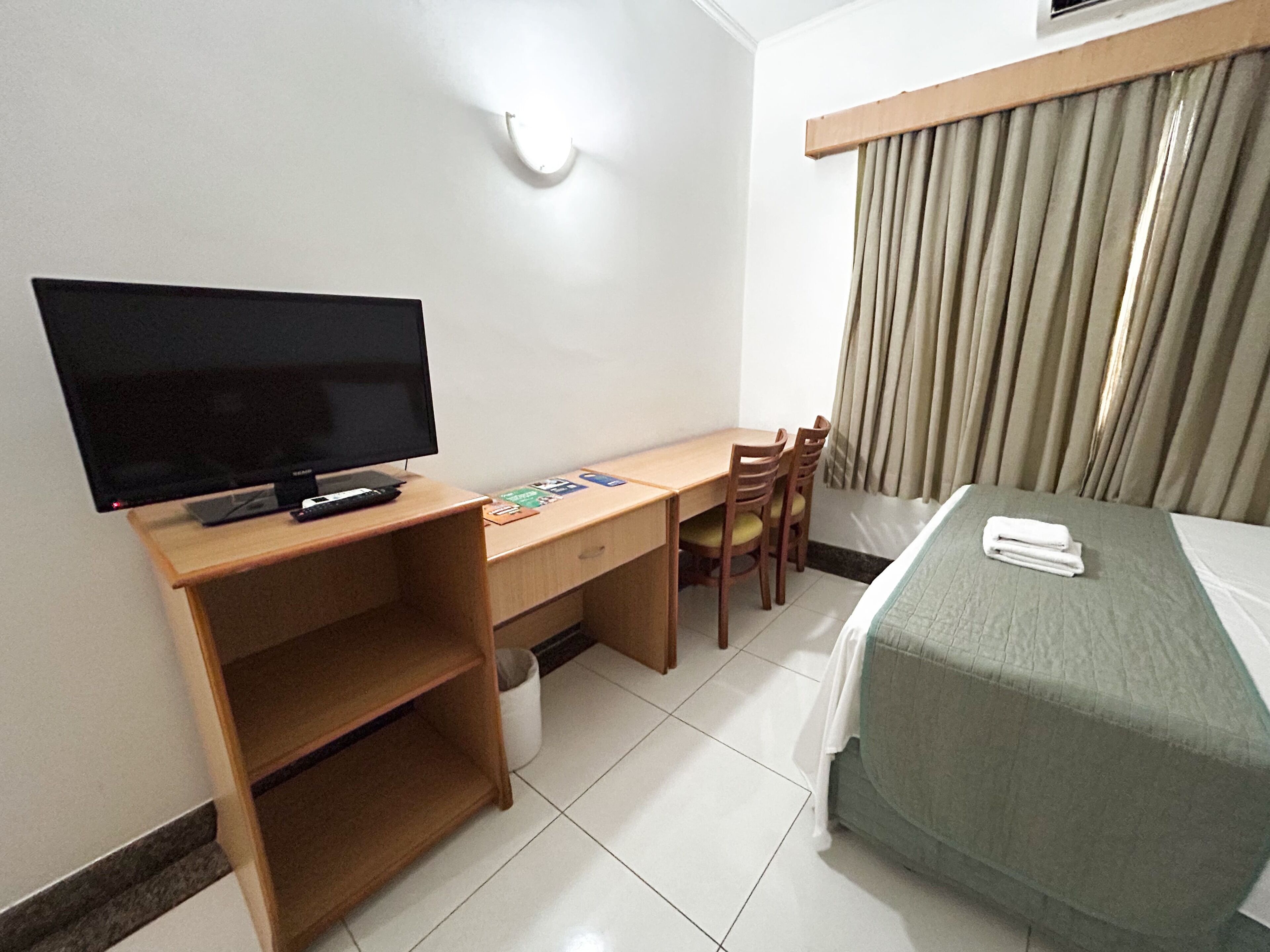 Una habitación de hotel con cama, escritorio con televisor y una silla.