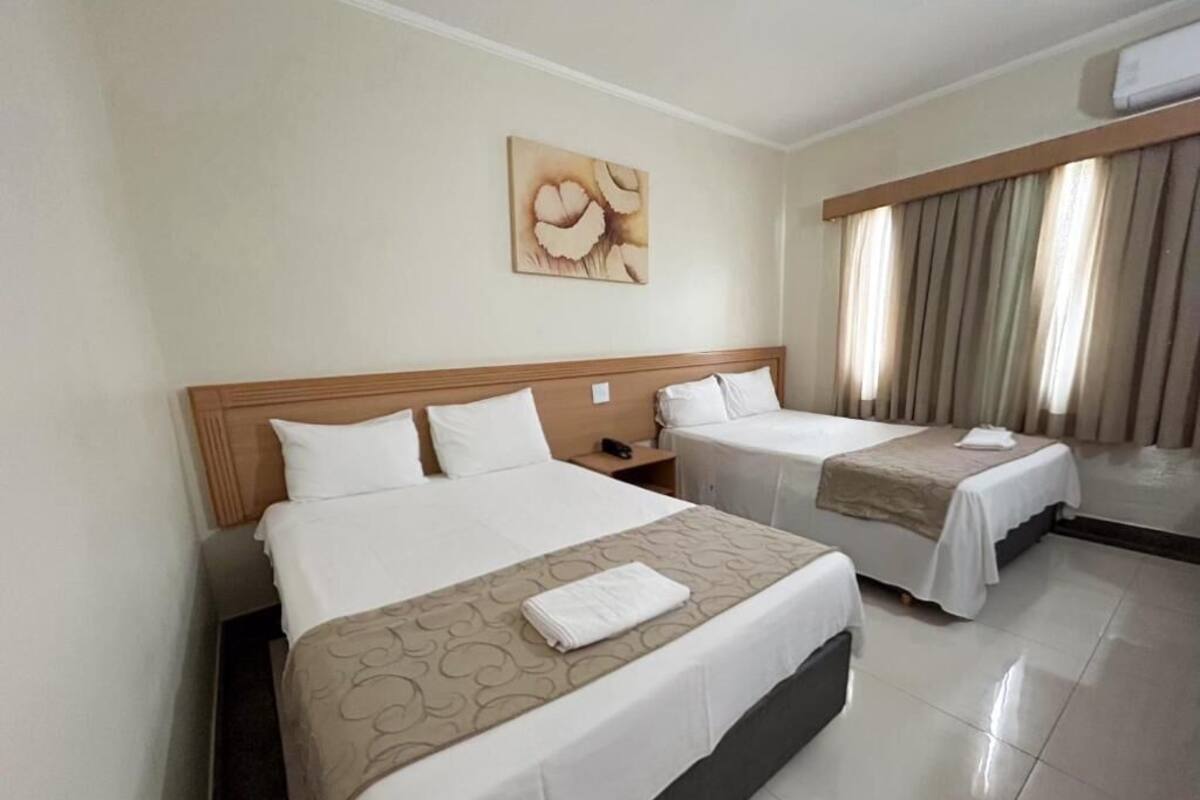 Habitación de hotel con dos camas, cabeceras, mesitas de noche, un cuadro en la pared y una ventana con cortinas.