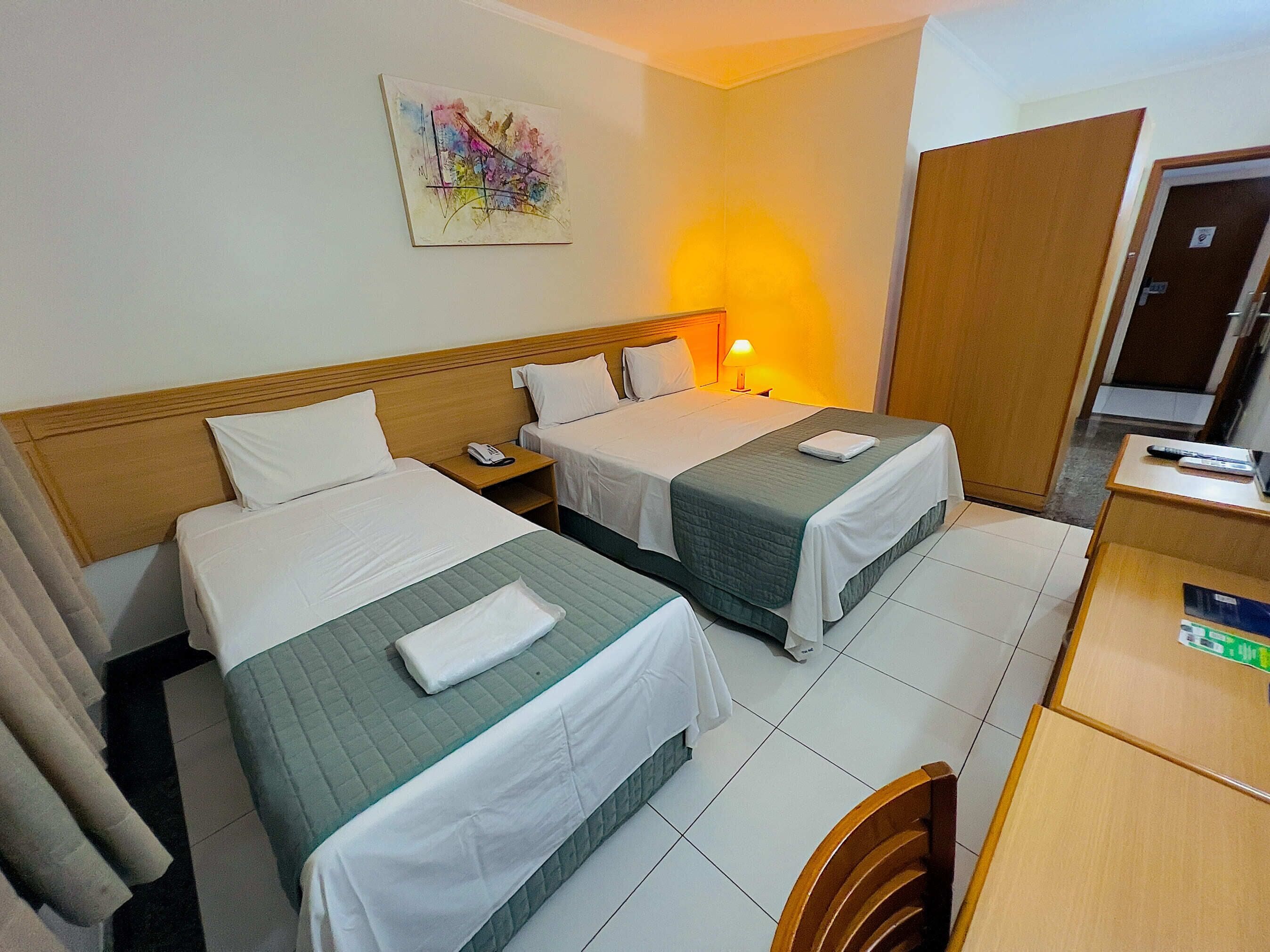A hotel room with two beds, a desk, a chair, a nightstand with a phone, and a painting on the wall.