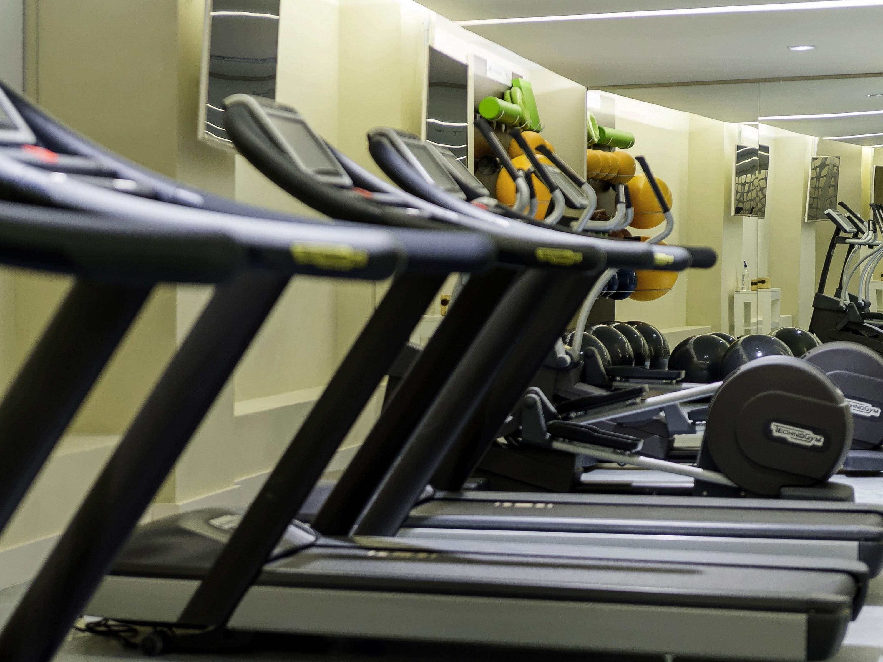 Een rij loopbanden in een sportschool, met krachtapparaten en gewichten op de achtergrond.