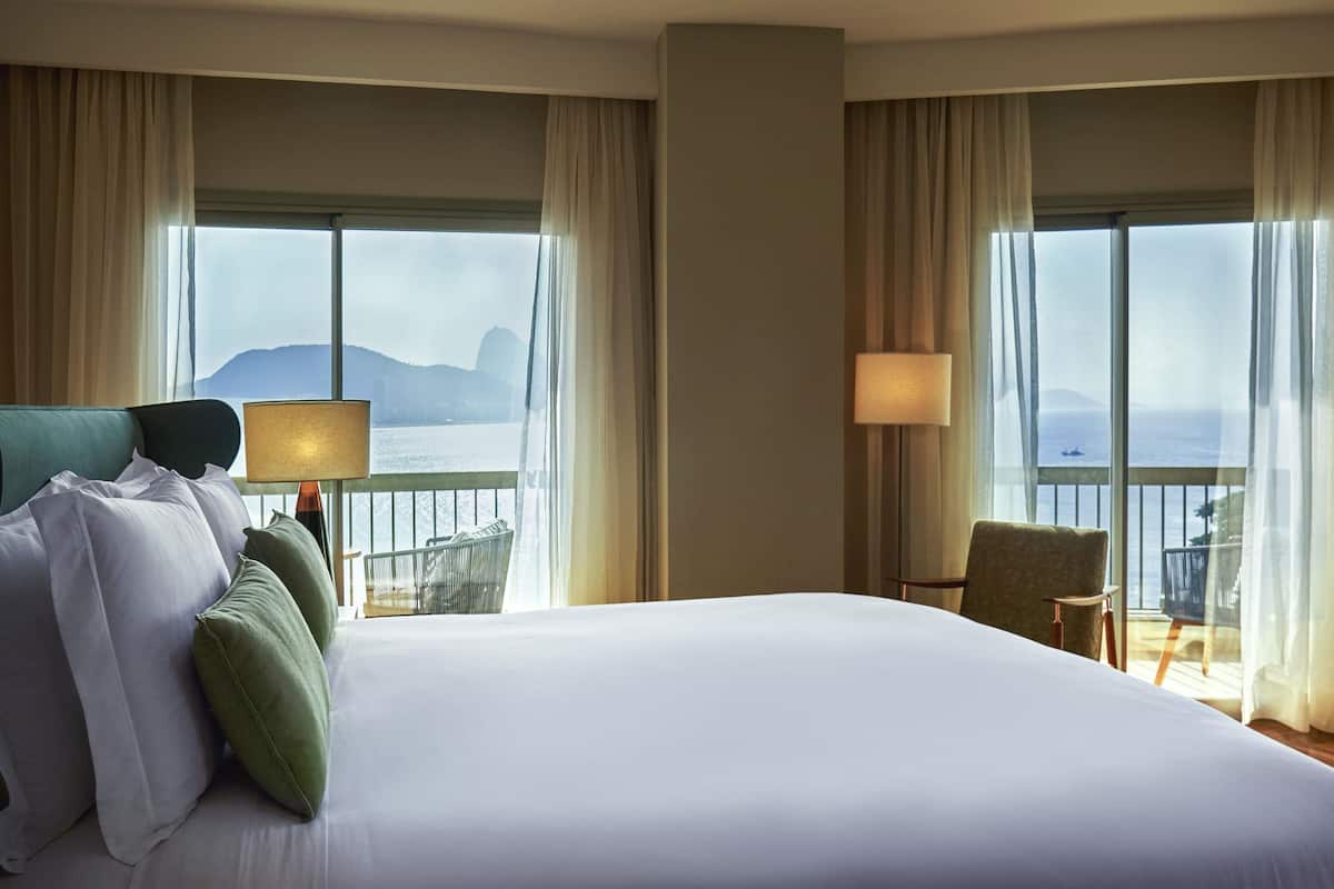 Ein Hotelzimmer mit einem großen Bett, zwei Stühlen, einer Lampe und Meerblick.