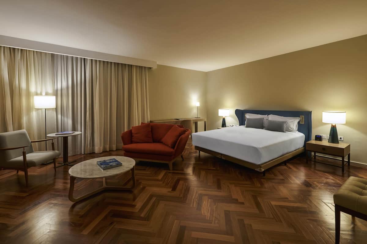 Ein Hotelzimmer mit einem Bett, zwei Stühlen, einem kleinen Tisch, einem Schreibtisch und einer Lampe.