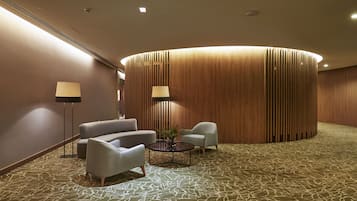Eine moderne Lobby mit einer gewölbten Holzwand, zwei Sesseln, einem runden Couchtisch und einem gemusterten Teppich.