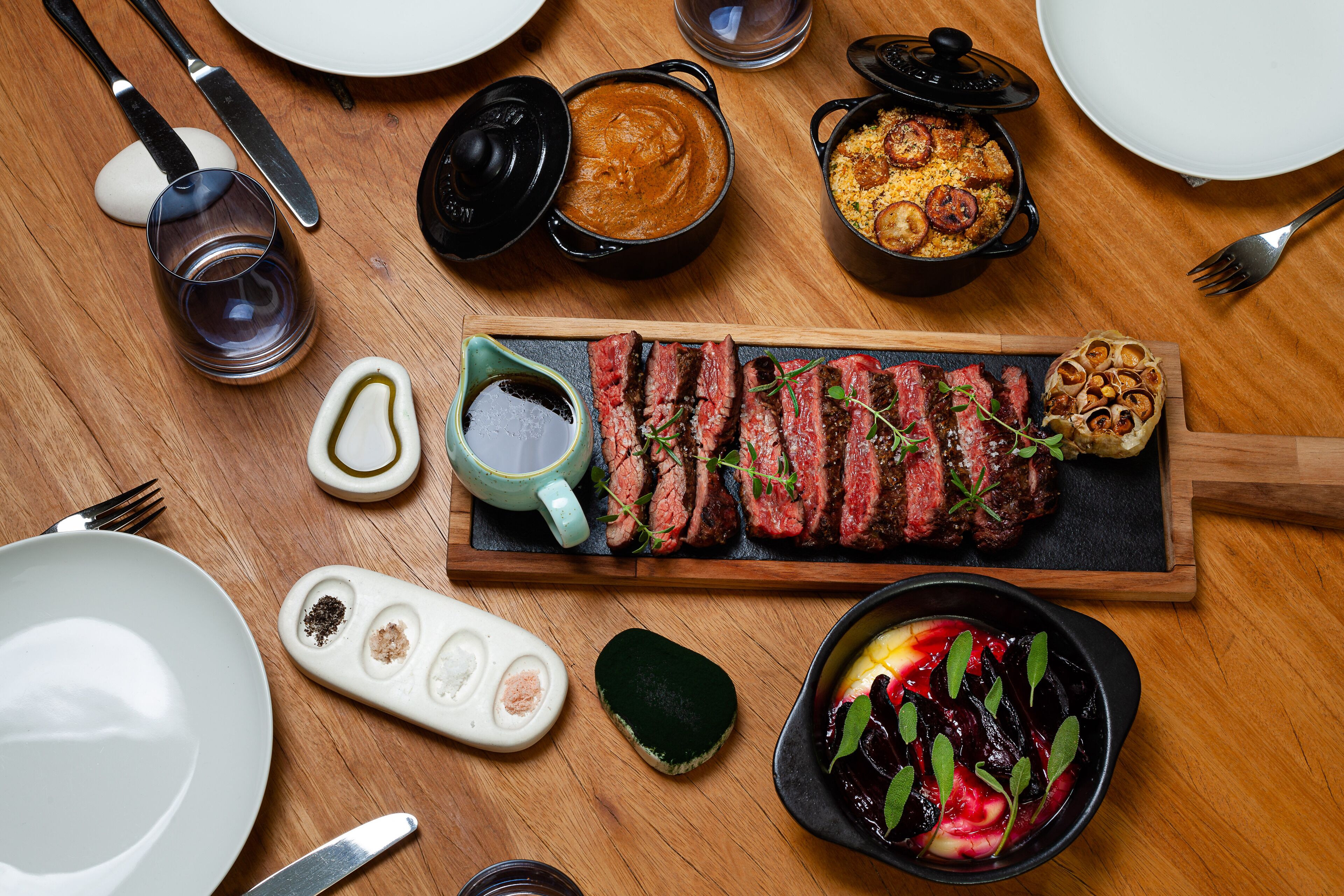 Una mesa de madera con una variedad de platos, incluyendo carne, verduras y salsas.